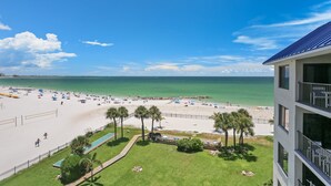 A beach view from a hotel balcony with a pool, palm trees, and a clear sky.