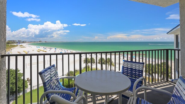 A balcony with a view of a beach, featuring a table and chairs.