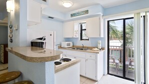 Une cuisine dotée d’un îlot central, d’un four à micro-ondes, d’un évier et d’une cuisinière. Une porte-fenêtre coulissante donne accès à un balcon aménagé avec des chaises.