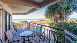 A balcony with a table and chairs, overlooking a beach with palm trees and a view of the ocean. - 🌊 Direct Gulf Front — Gulf Strand Resort, St. Pete Beach (St Pete Beach)