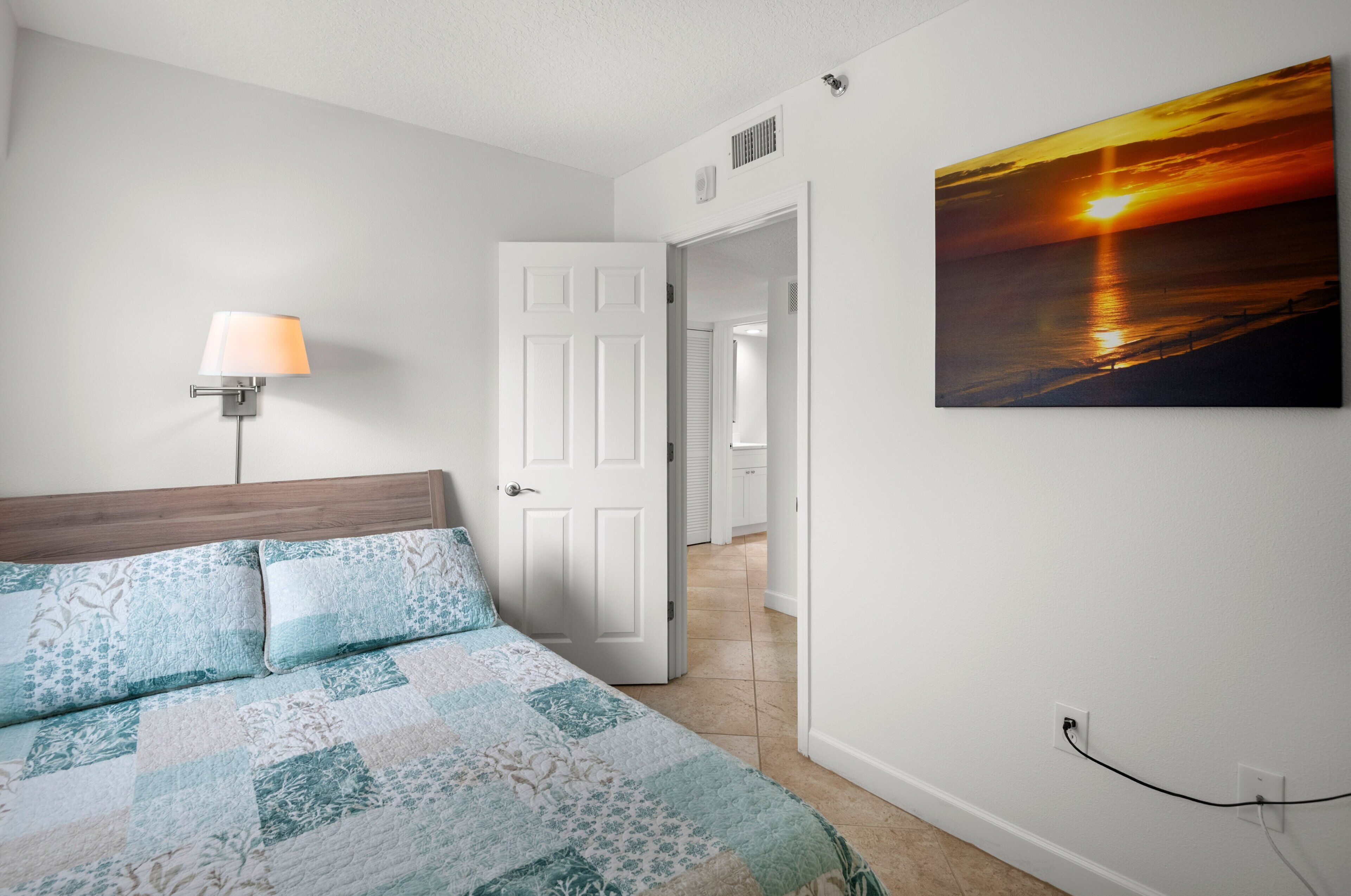 A bedroom with a bed, a nightstand, a lamp, and a painting of a sunset.