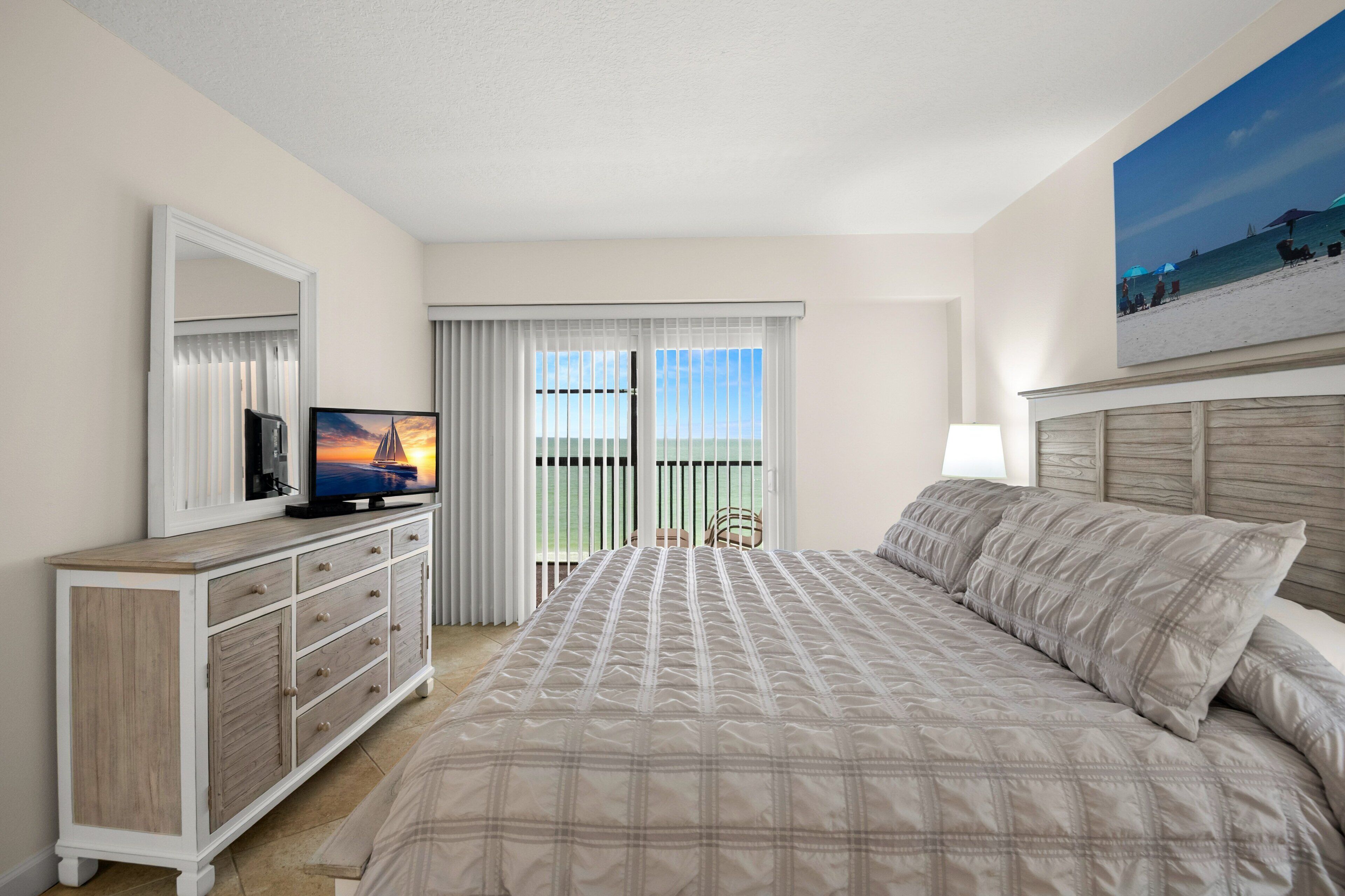 Une chambre à coucher avec un lit, un téléviseur posé sur une commode, une chaise et une fenêtre avec des rideaux.