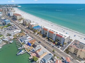 An aerial view of a coastal city with a marina, a beach, and a hotel with multiple floors and balconies.