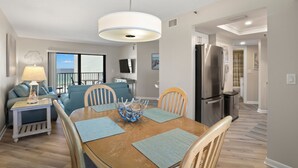 Zona de menjador amb taula de fusta, sobreades blaus i un bol decoratiu. Al fons, hi ha un sofà i una làmpada.