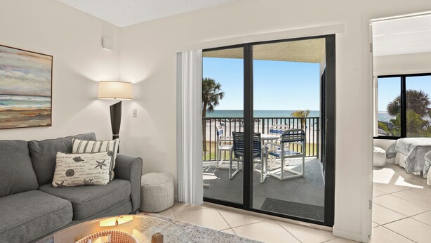 A living room with a grey sofa, a lamp, and a view of a balcony with outdoor furniture.