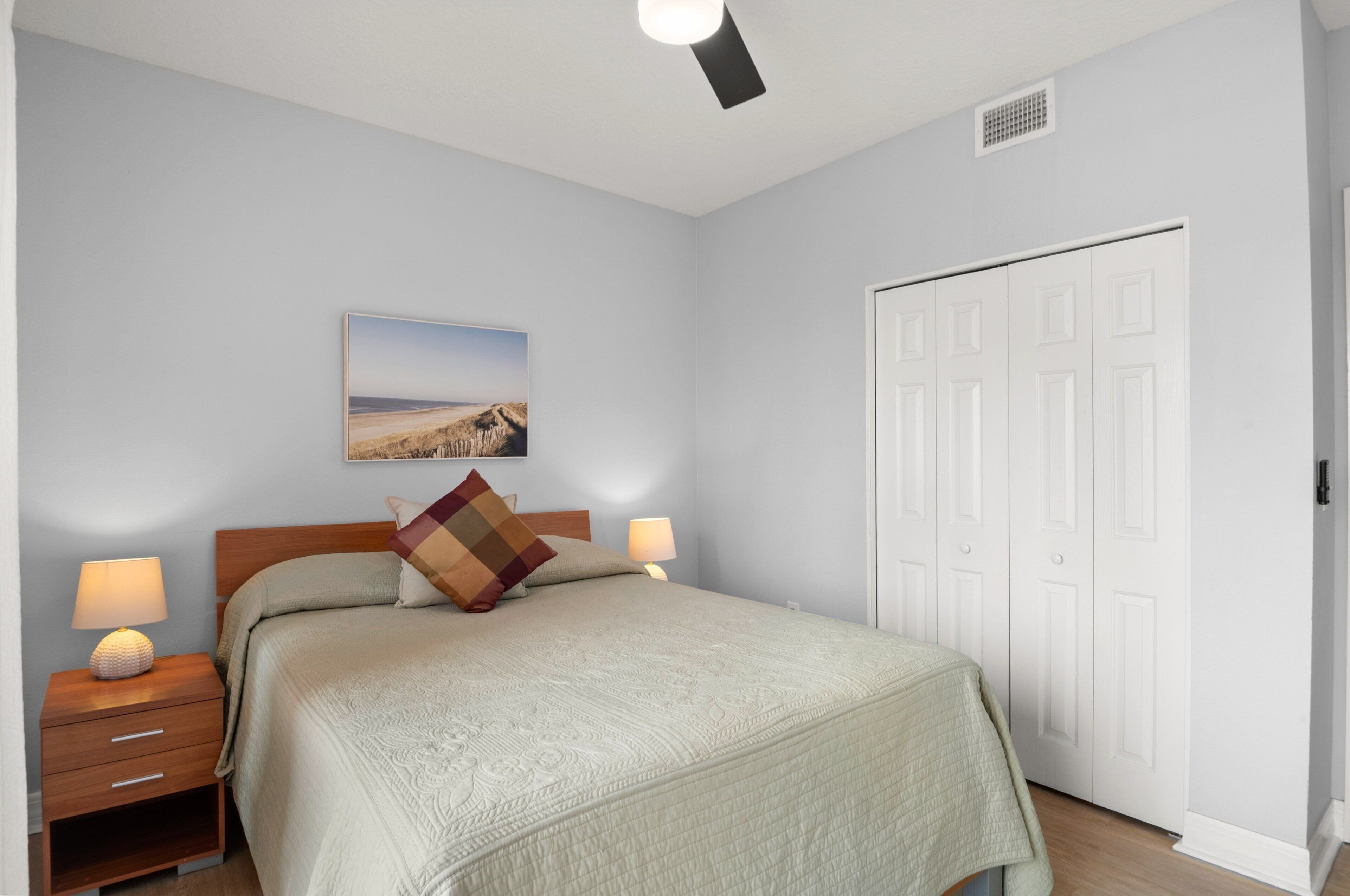 A bedroom with a bed, nightstands, a lamp, a picture on the wall, and a closet.
