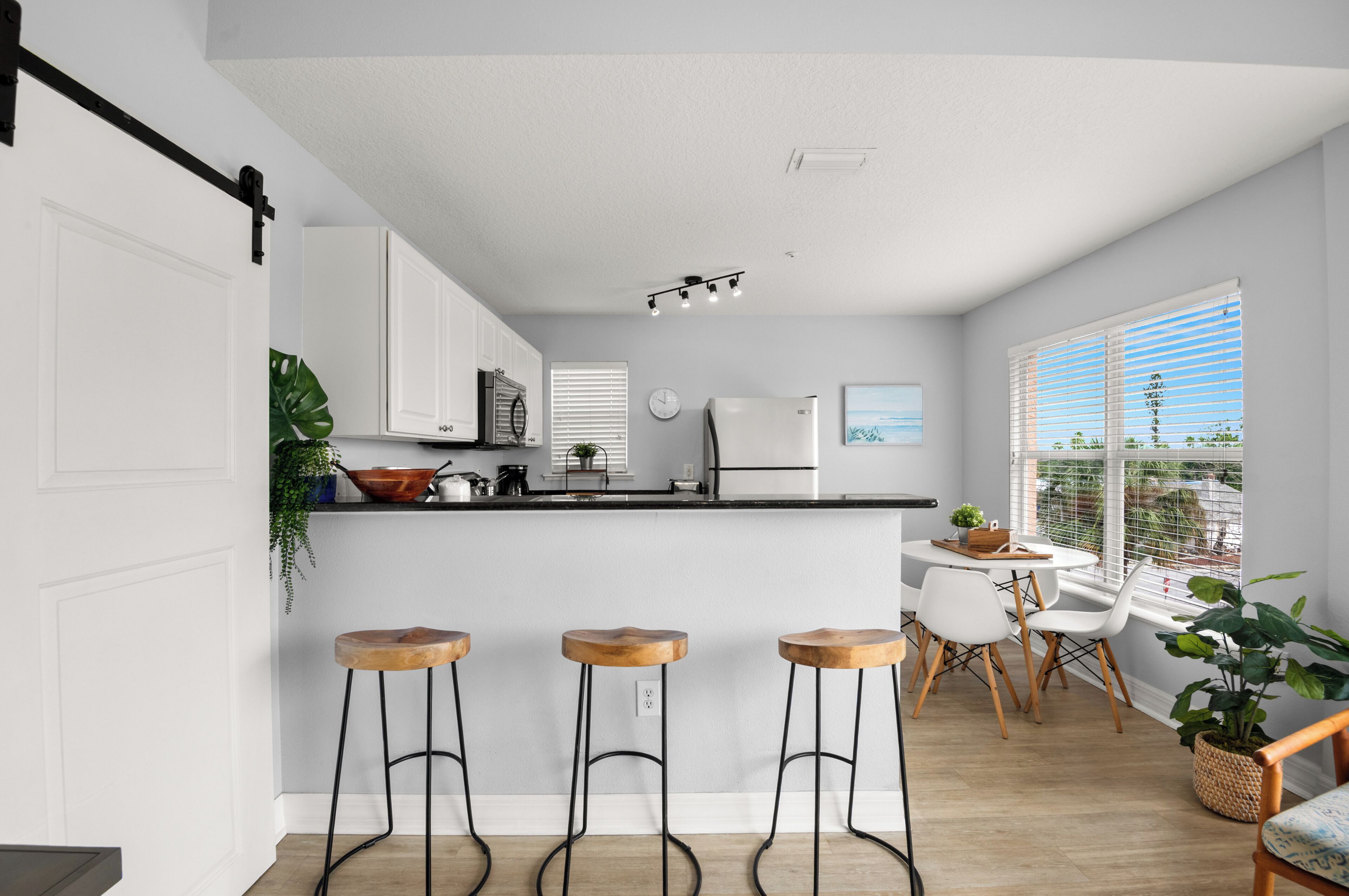 Une cuisine moderne avec des meubles blancs, un îlot central, des tabourets de bar et un coin repas avec des chaises blanches.