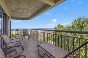 A balcony with wicker chairs, a table, and a view of the ocean.