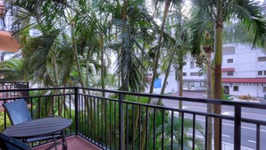 A balcony with a table and chairs, surrounded by palm trees and a view of a street.