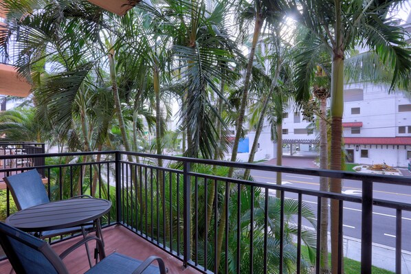 A balcony with a table and chairs, surrounded by palm trees and a view of a street.