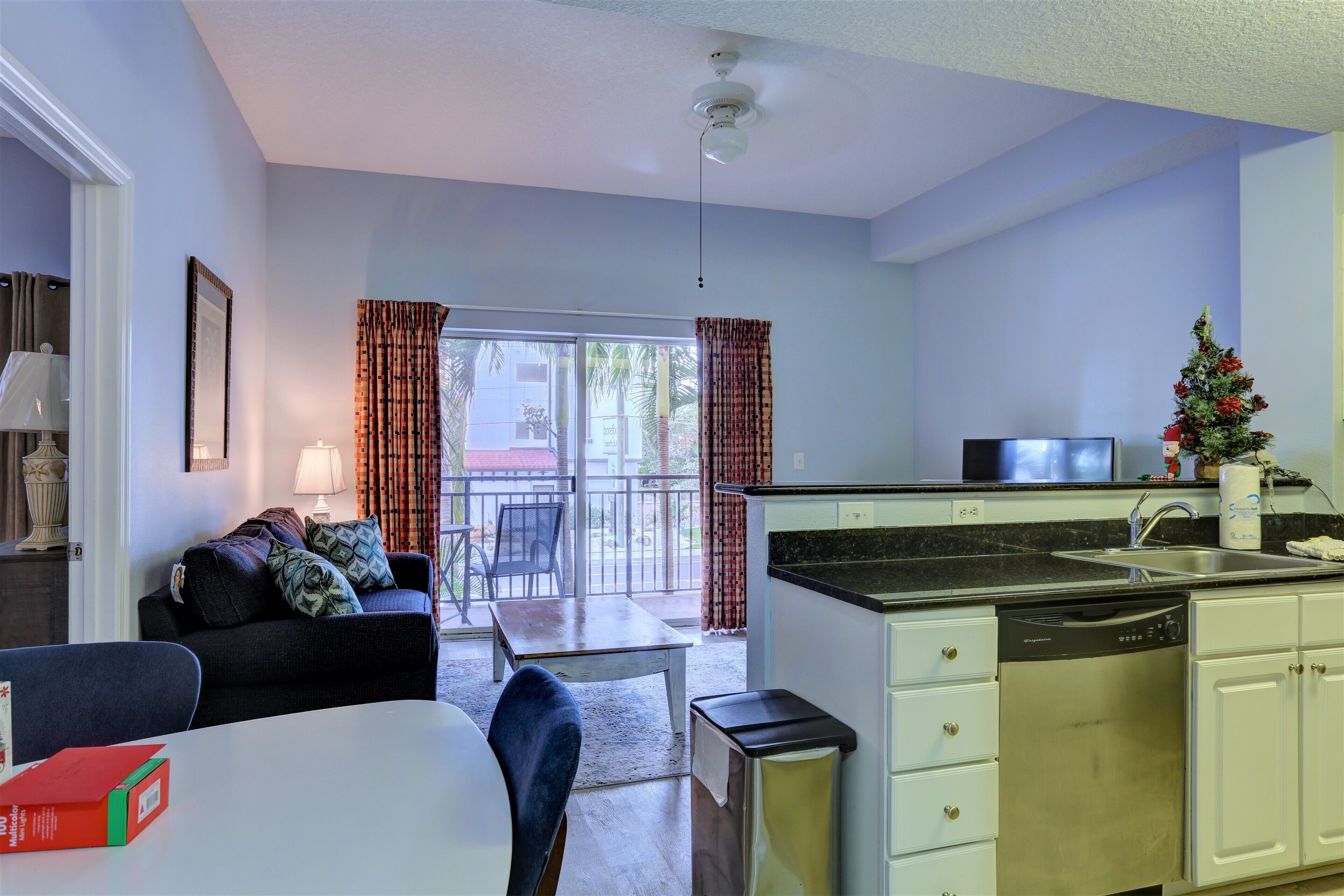 A compact living space with a kitchenette, dining area, and a balcony with curtains.