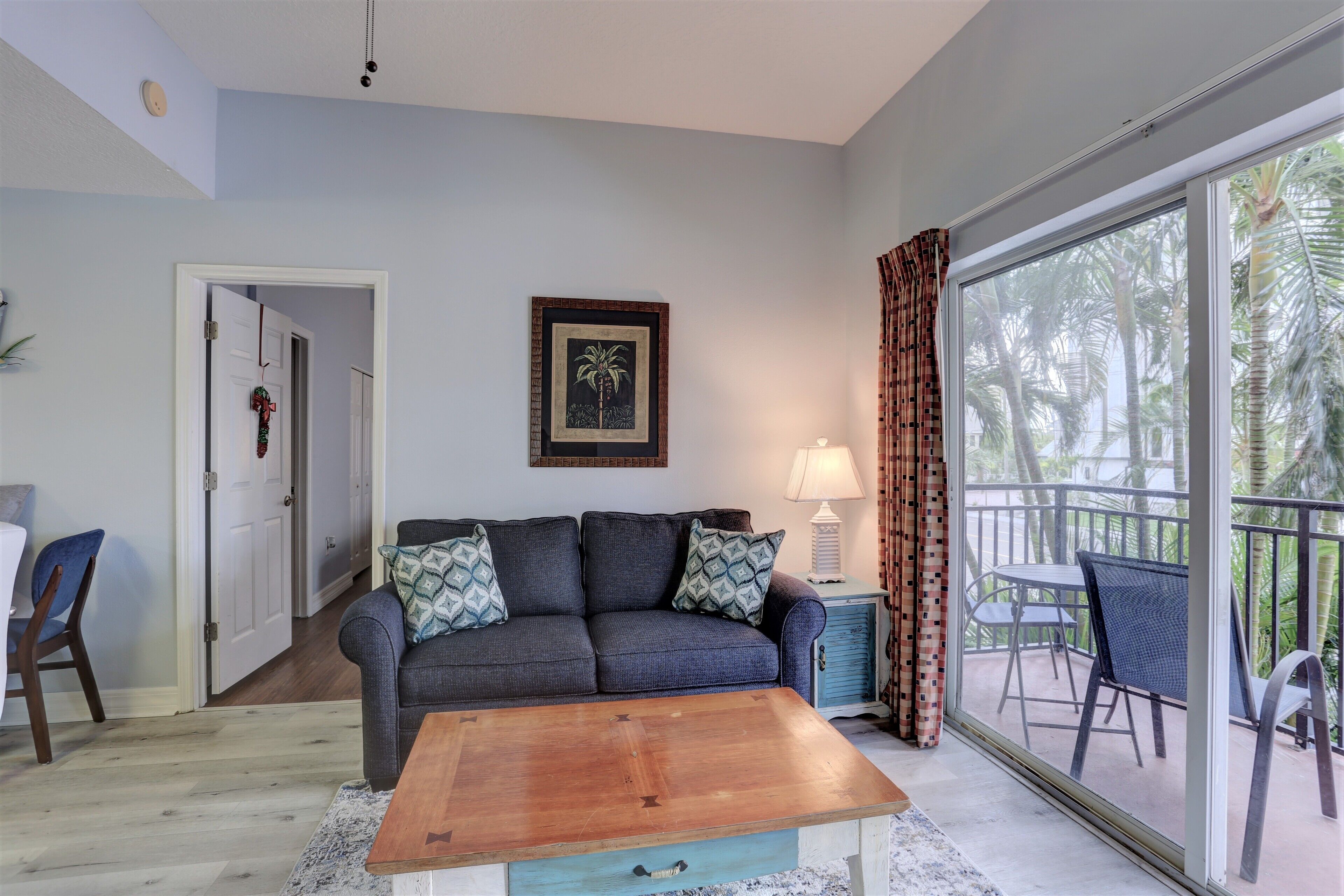 A living room with a sofa, coffee table, and a view of a balcony with outdoor furniture.