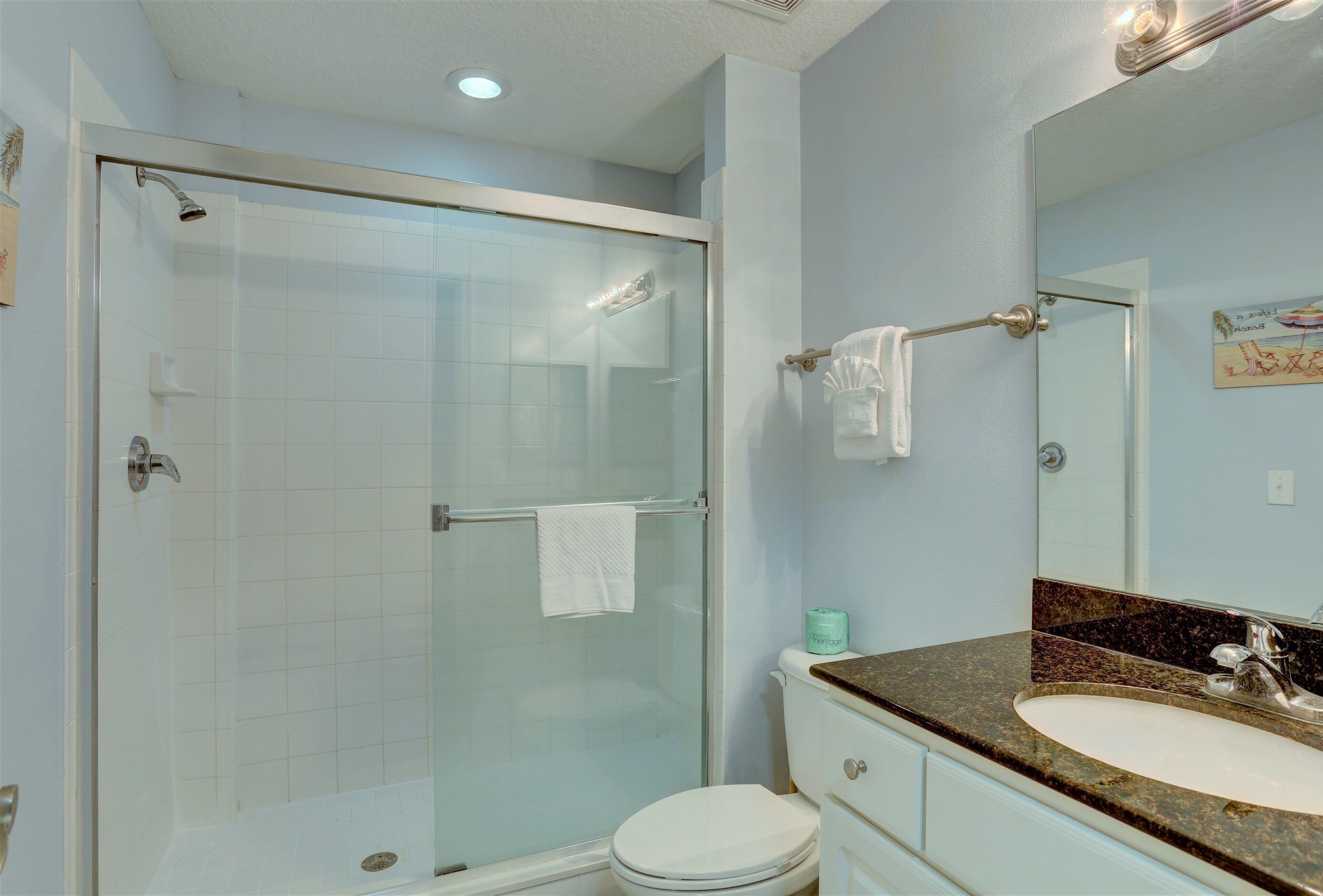 A bathroom with a glass-enclosed shower, a white toilet, a sink with a granite countertop, and a mirror above the sink.