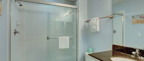A bathroom with a glass-enclosed shower, a white toilet, a sink with a granite countertop, and a mirror above the sink.