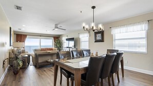 A spacious living room with a dining area, a ceiling fan, and a large window with blinds.