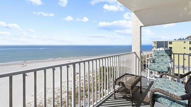 A balcony with wicker furniture overlooking a beach and ocean.