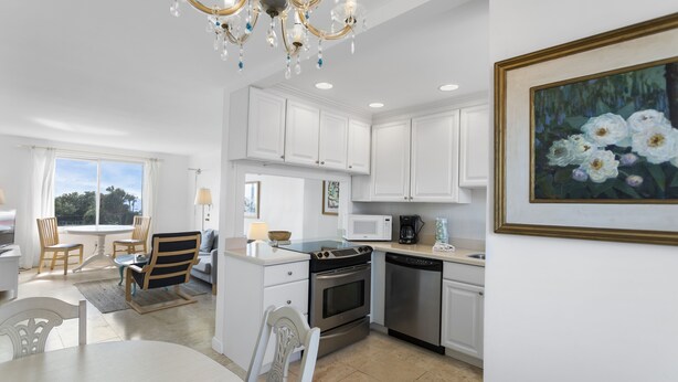 A modern kitchen with white cabinets, stainless steel appliances, a dining area with a table and chairs, and a chandelier.
