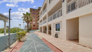 A courtyard with a shuffleboard court, a covered seating area, and a building with balconies.