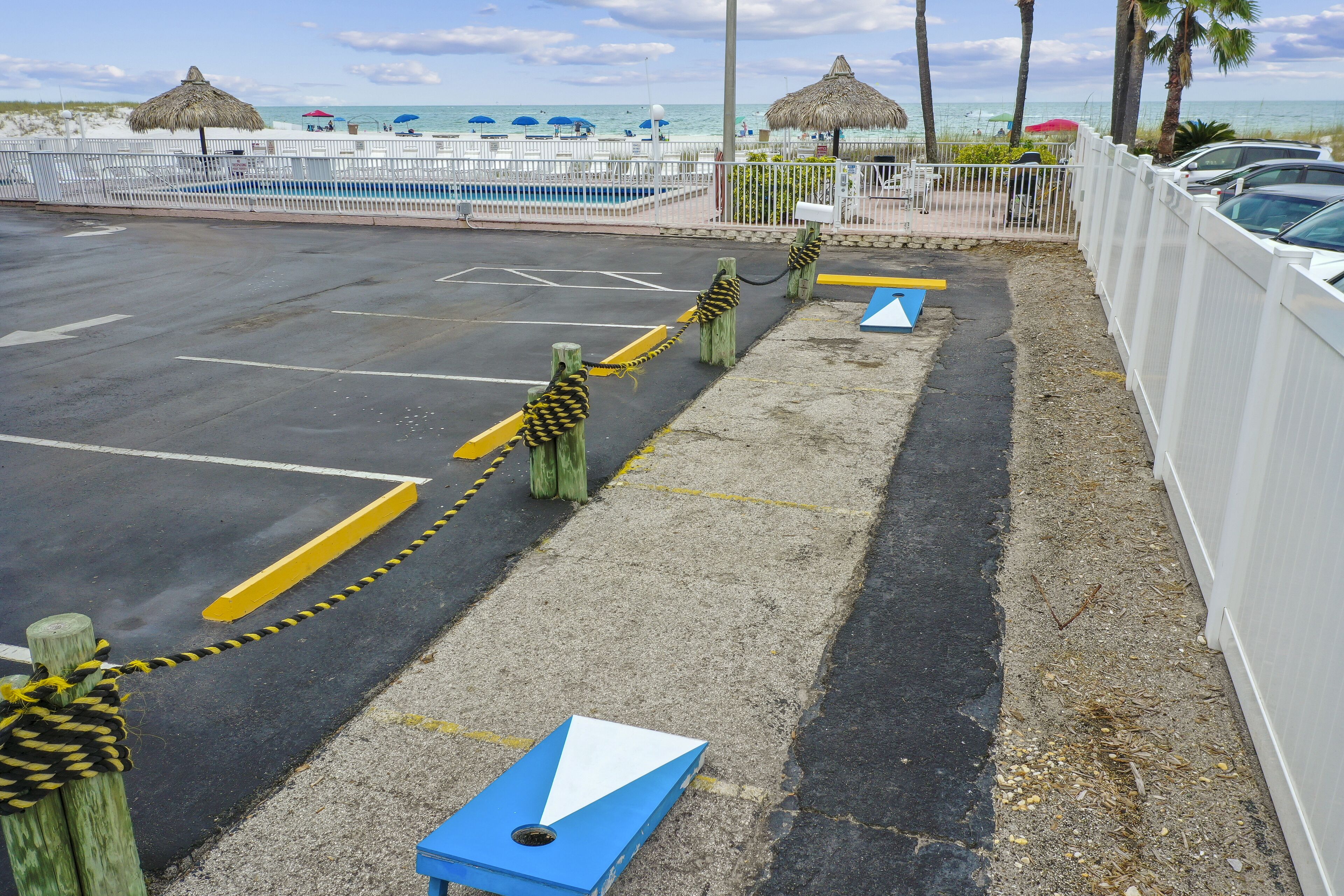 Ein Parkplatz mit gelb-schwarz gestreiften Absperrungen, einem blauen Pfeil als Richtungshinweis und einem weißen Zaun.