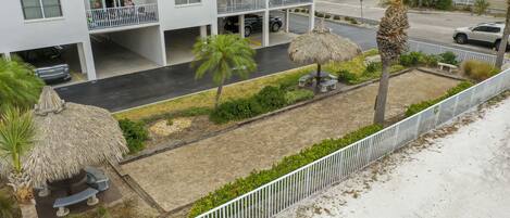 Un hotel de varios pisos con balcones, un estacionamiento y un jardín ajardinado con palmeras y una estructura con techo de paja.