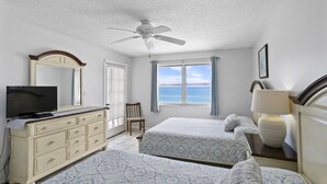 Une chambre avec deux lits, un ventilateur de plafond, une télévision, une commode et une vue sur l’océan.