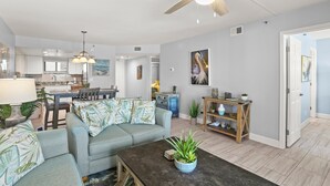 A spacious living room with a ceiling fan, a dining area with a table and chairs, and a kitchen in the background.