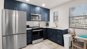 A modern kitchen with dark blue cabinets, stainless steel appliances, a microwave, and a window with blinds.