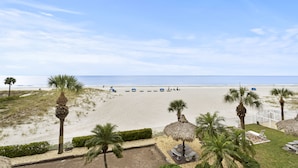 A beach view with palm trees, a fenced area with seating, and a clear sky.