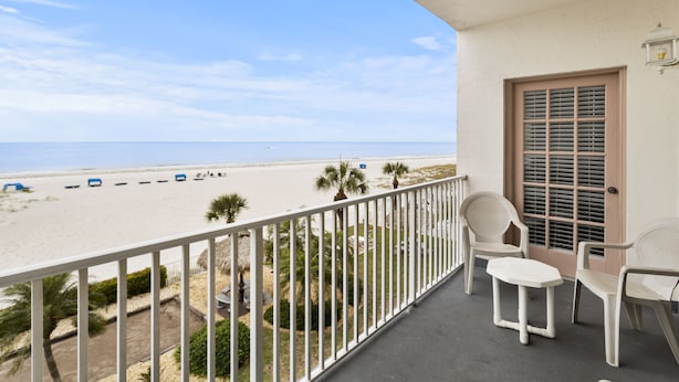 A balcony with a view of the beach, white chairs, and a door with shutters.