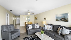 A living room with a grey sofa set, a coffee table, and a dining area in the background.