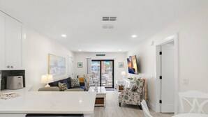 A modern living room with a sofa, a dining table, and a kitchen area with a dishwasher.