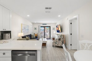 A modern living room with a sofa, a dining table, and a kitchen area with a dishwasher.