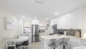 A modern kitchen with white cabinetry, a stainless steel refrigerator, a microwave, and a large island with bar stools.