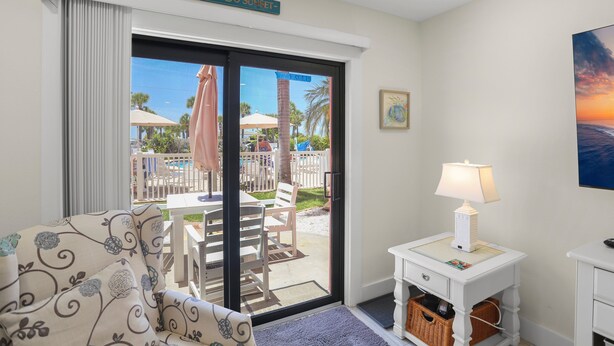 A room with a view of a pool, a chair, a table, a lamp, and a painting on the wall.