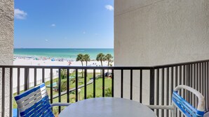 A balcony with a view of a beach, a table, and two chairs. - 🌅 Caprice Resort Unit #303 – Gulf Front Escape for Up to Four Guests (St Pete Beach)