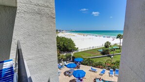 A balcony with a view of a beach, poolside lounge chairs, and umbrellas. - 🌅 Caprice Resort Unit #303 – Gulf Front Escape for Up to Four Guests (St Pete Beach)