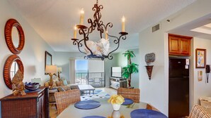 A dining area with a chandelier, round mirrors, wicker furniture, and a view to the outside. - 🌅 Caprice Resort Unit #303 – Gulf Front Escape for Up to Four Guests (St Pete Beach)