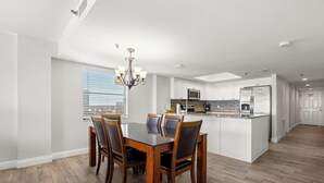 Una cocina moderna con armarios blancos, una isla central y una zona de comedor con mesa y sillas de madera.