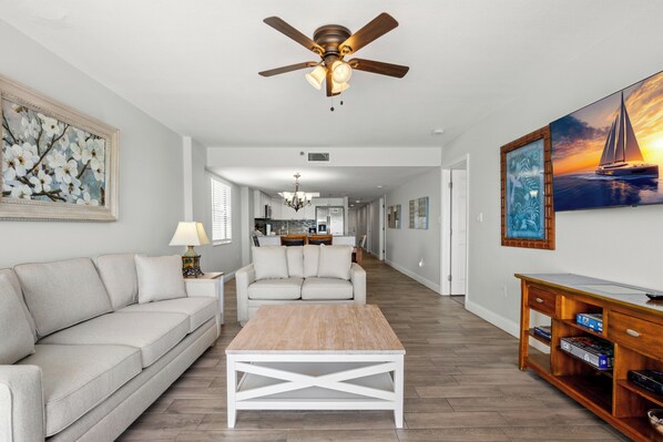 A living room with a ceiling fan, a sofa, a coffee table, and artwork on the walls.