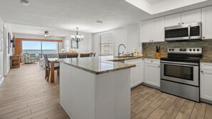 Cocina moderna con armarios blancos, una isla grande, electrodomésticos de acero inoxidable y un comedor con vistas.