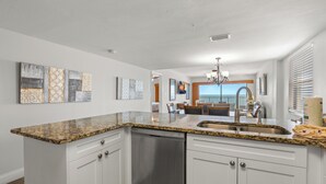 Una cocina con encimeras de granito, muebles blancos, lavavajillas y un comedor con candelabro.