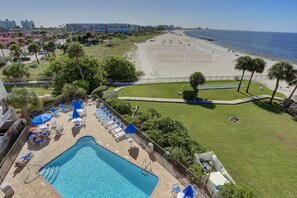 A pool area with lounge chairs and umbrellas, a beach with volleyball courts, and a view of the ocean.