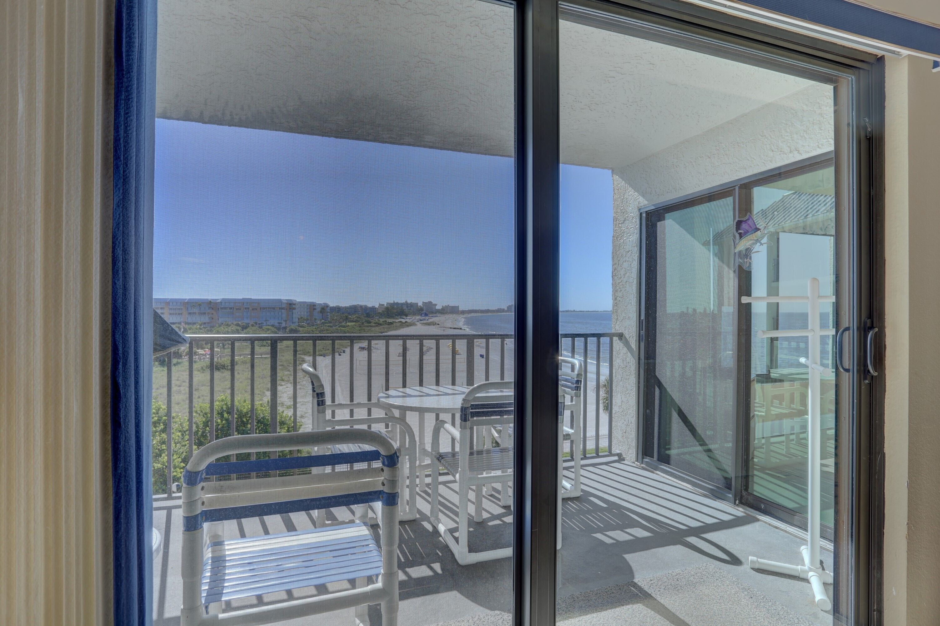 A balcony with a view of the beach, a table, and chairs.