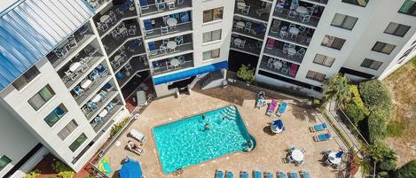 A multi-story building with a rooftop pool area, outdoor seating, and a landscaped garden.