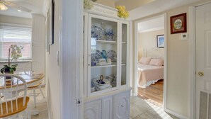A room with a dining area, a glass-fronted cabinet with dishes, a bed, and a door leading to another room.