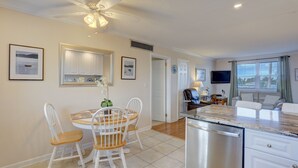 A modern kitchen with white cabinetry, a dining table with chairs, a ceiling fan, and a built-in dishwasher.