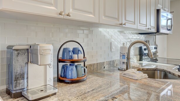 A kitchen with white cabinets, a coffee maker, a kettle, and a sink.