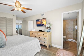 Un dormitorio con cama, ventilador de techo, cómoda, televisor y baño con ducha e inodoro.