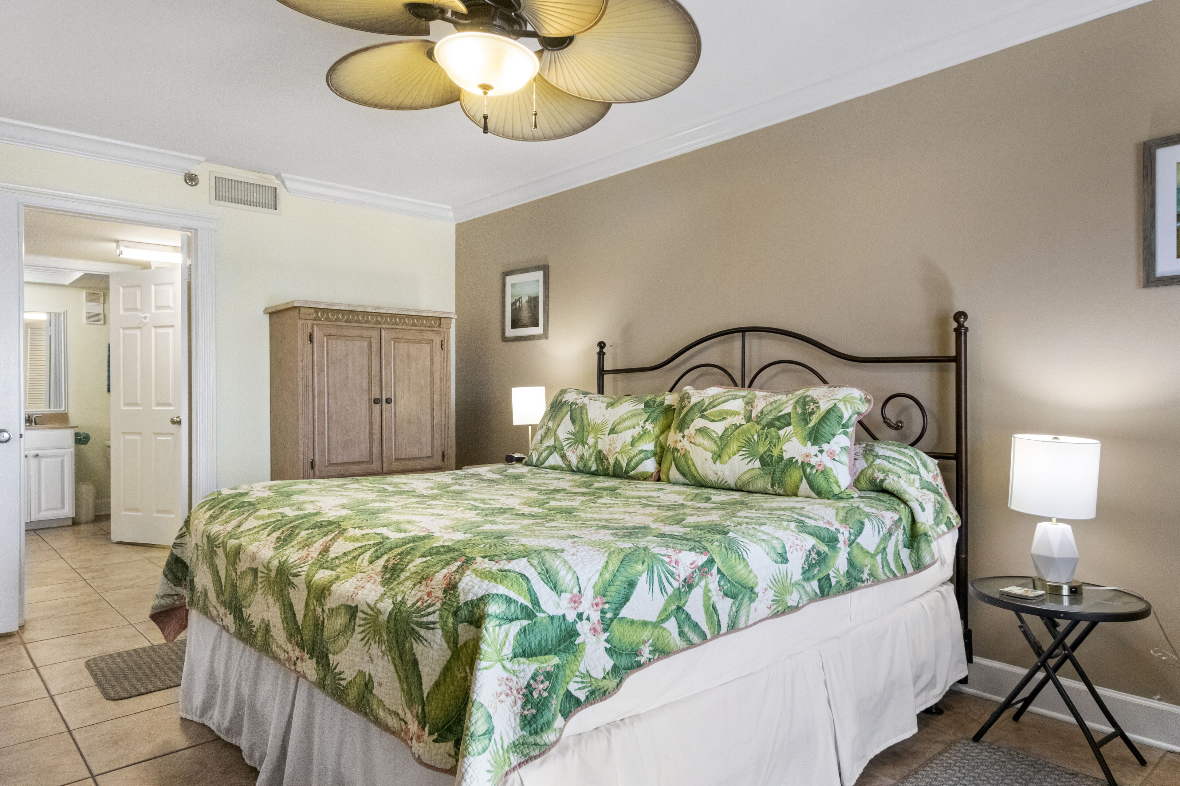 A bedroom with a bed, a nightstand, a ceiling fan, a door, and a cabinet.
