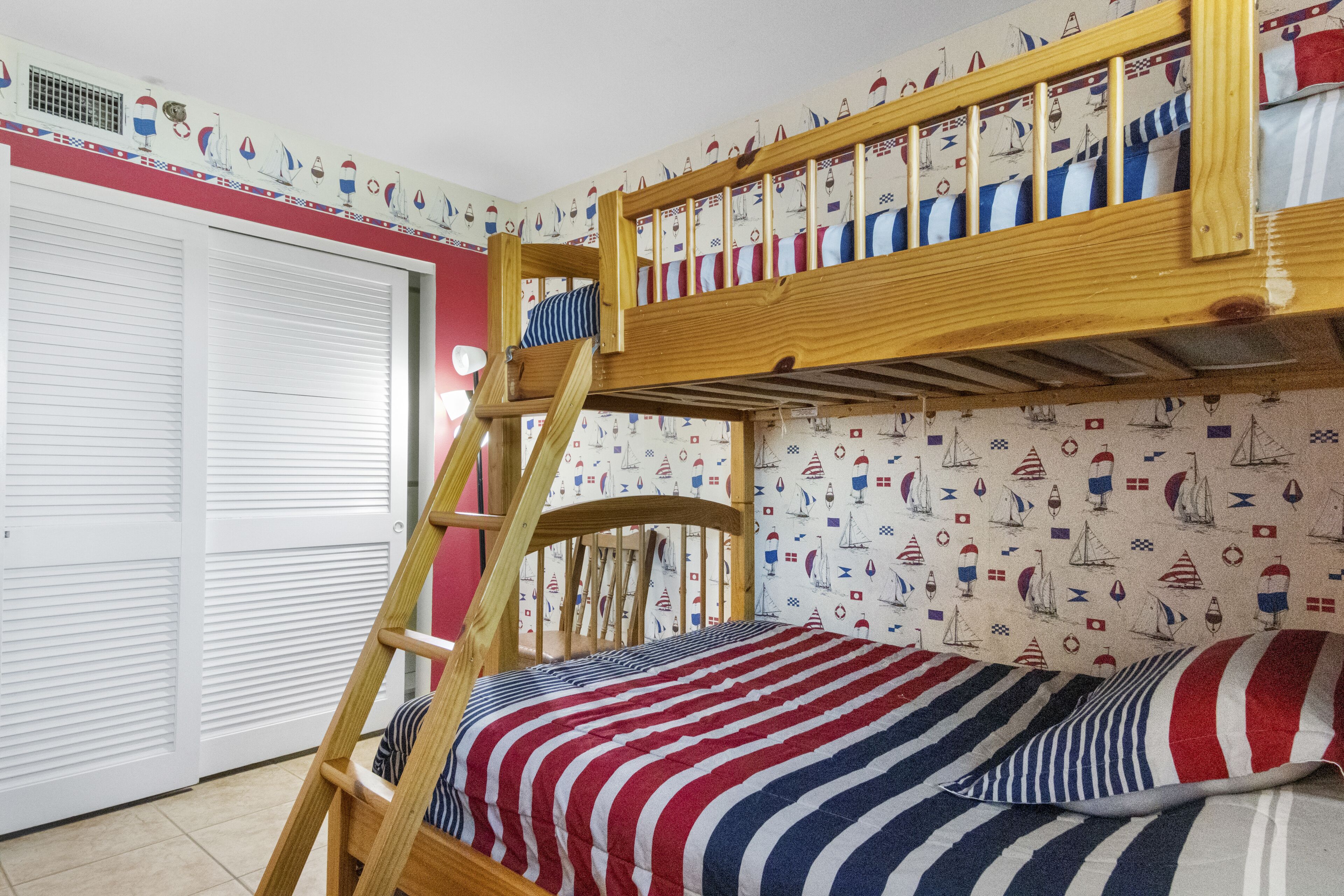 Een stapelbed met een gestreept dekbedovertrek, een houten ladder en een kast met witte luiken.